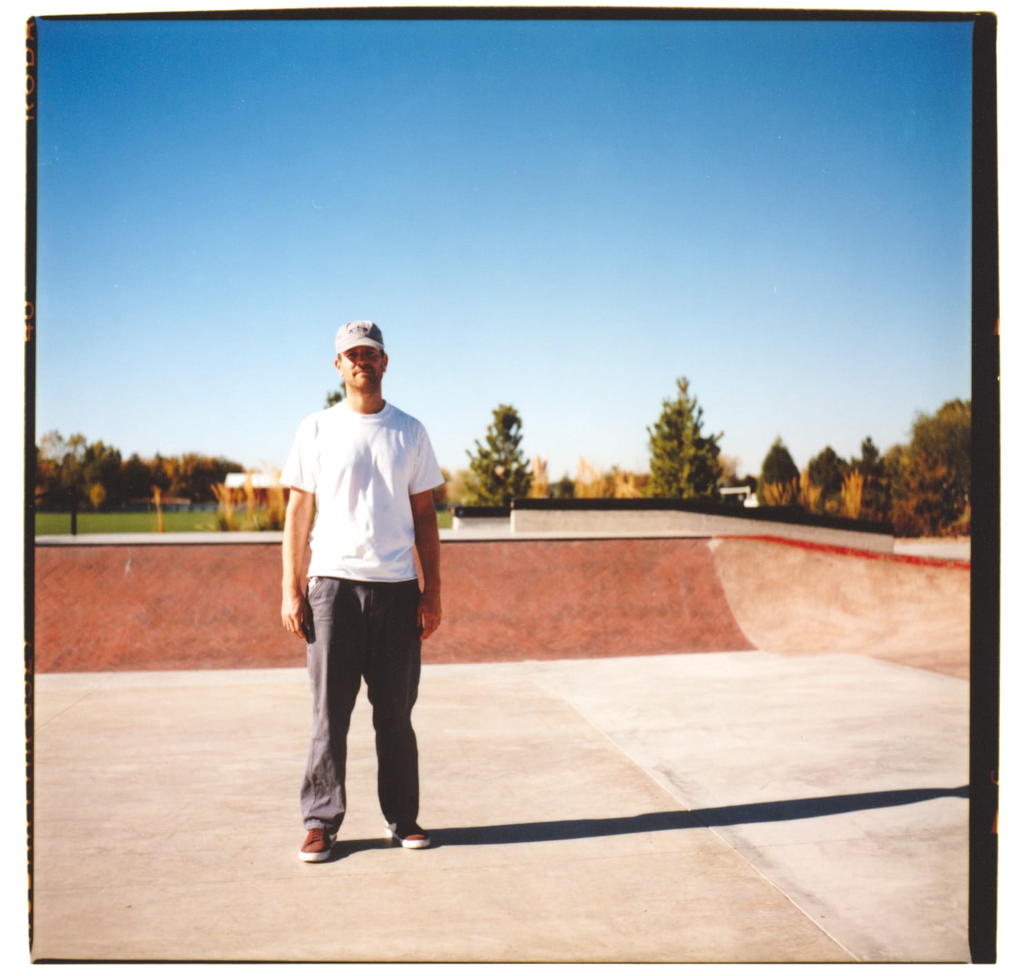 1 guy standing in an empty skatepark. The ramps are red and the sky is blue.